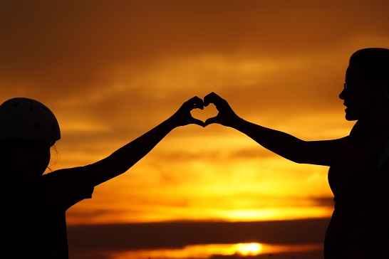 people make heart symbol with hands beneath the setting sun