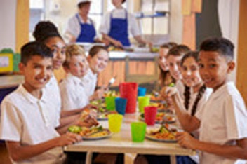 Kids At A Table In A Primary School Cafeteria Look To Camera